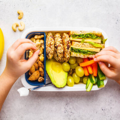 School healthy lunch box with sandwich, cookies, nuts, fruits and avocado on a white background.